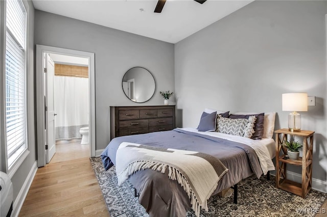 bedroom featuring ensuite bath, light wood-style flooring, baseboards, and a ceiling fan