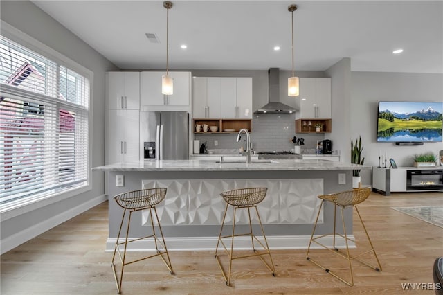 kitchen with stainless steel fridge, a sink, wall chimney range hood, and a breakfast bar area