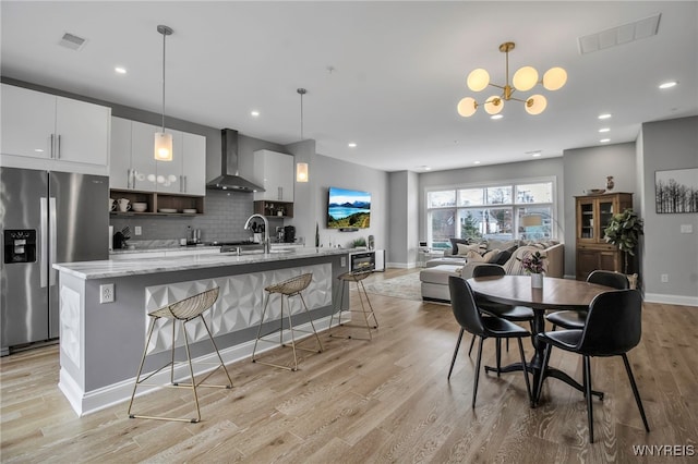 kitchen with wall chimney range hood, backsplash, stainless steel fridge, and visible vents