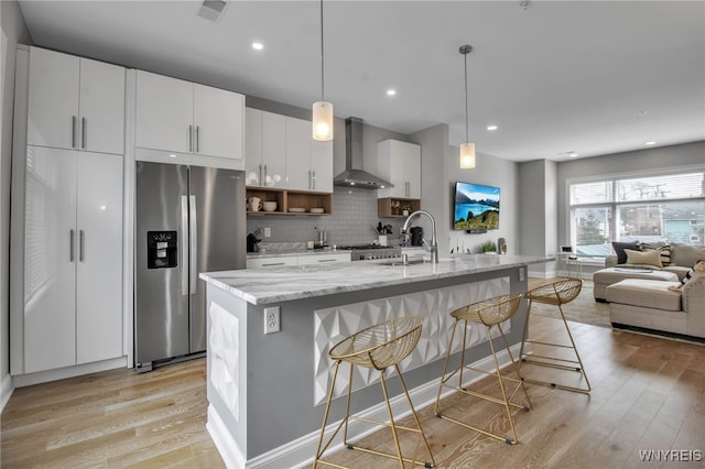 kitchen with wall chimney range hood, a sink, light wood-style flooring, and stainless steel fridge with ice dispenser