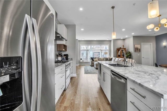 kitchen featuring light wood finished floors, white cabinets, open floor plan, stainless steel appliances, and a sink