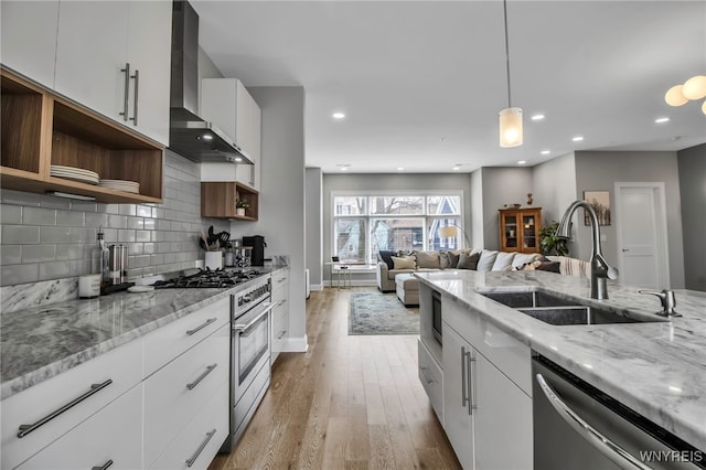 kitchen featuring tasteful backsplash, wall chimney exhaust hood, appliances with stainless steel finishes, open shelves, and a sink