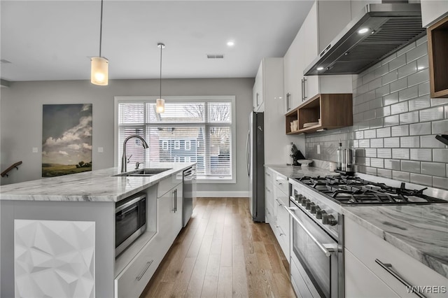 kitchen featuring a center island with sink, visible vents, stainless steel appliances, wall chimney range hood, and a sink