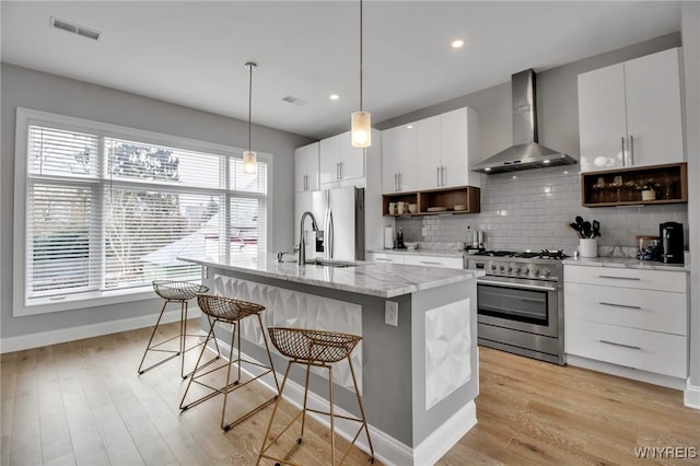 kitchen with stainless steel appliances, a breakfast bar, a sink, visible vents, and wall chimney exhaust hood