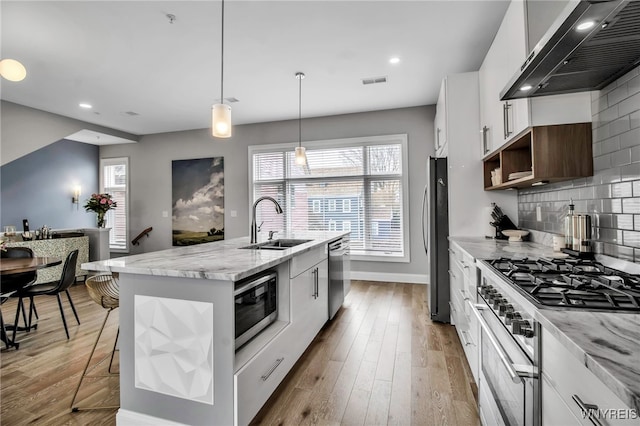 kitchen featuring extractor fan, a sink, visible vents, appliances with stainless steel finishes, and a center island with sink