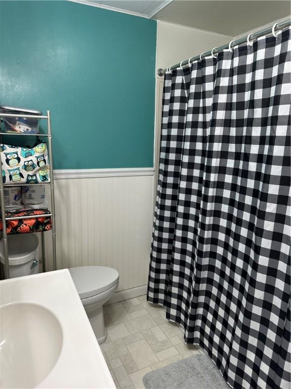 bathroom with toilet, a shower with curtain, a sink, and wainscoting