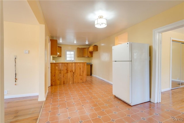 kitchen with a peninsula, baseboards, brown cabinets, and freestanding refrigerator