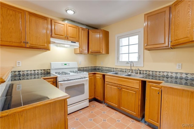 kitchen featuring brown cabinets, gas range gas stove, a sink, and under cabinet range hood