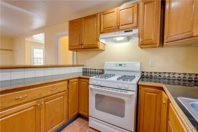 kitchen with brown cabinetry, tile counters, under cabinet range hood, and white gas range