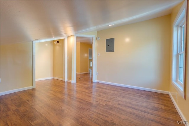 spare room with a wealth of natural light, wood finished floors, electric panel, and baseboards