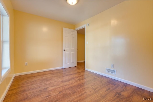 spare room with baseboards, visible vents, and wood finished floors