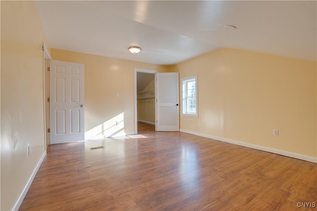 unfurnished room with lofted ceiling, visible vents, baseboards, and wood finished floors