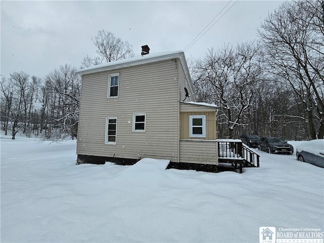 snow covered back of property with a wooden deck