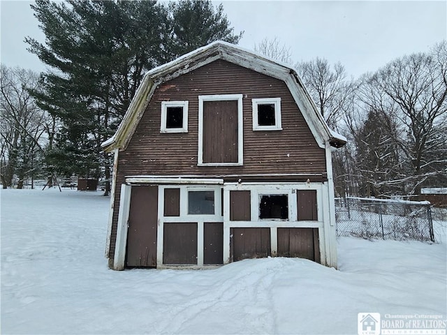 snow covered structure with a barn, fence, and an outbuilding