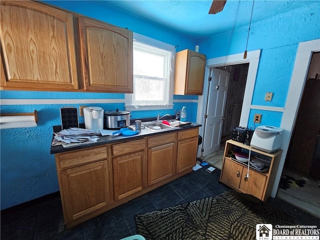 kitchen with dark tile patterned flooring, dark countertops, a sink, and a ceiling fan