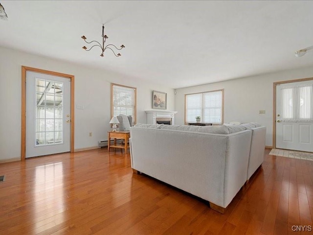 living area featuring a chandelier, a baseboard radiator, a fireplace, baseboards, and wood-type flooring