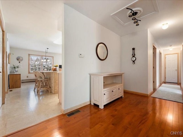 hallway featuring light wood finished floors, baseboards, visible vents, and a baseboard heating unit