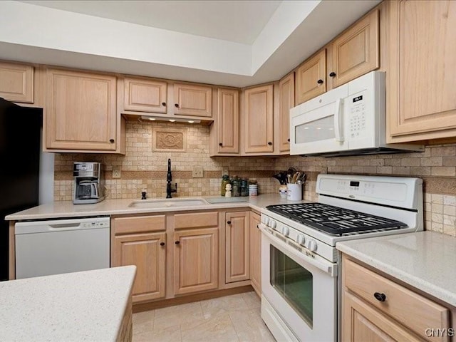 kitchen with light brown cabinetry, white appliances, a sink, and light countertops