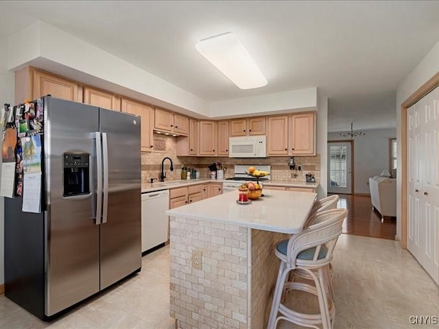 kitchen with white appliances, decorative backsplash, a kitchen island, light countertops, and a sink