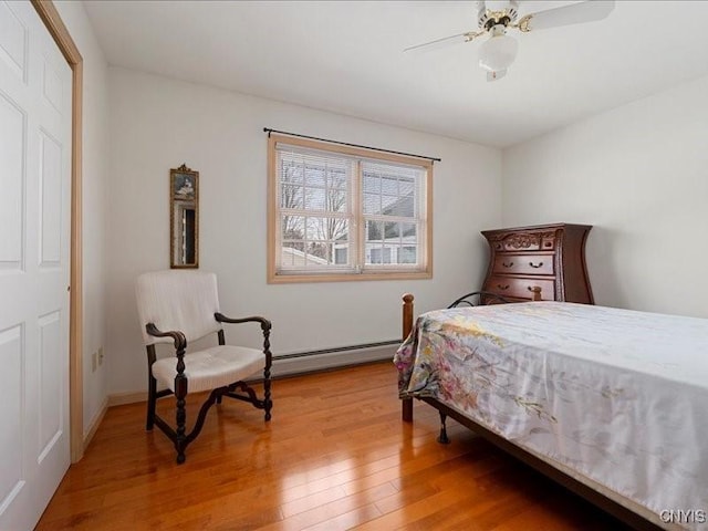 bedroom featuring light wood-style floors, a baseboard heating unit, and a ceiling fan