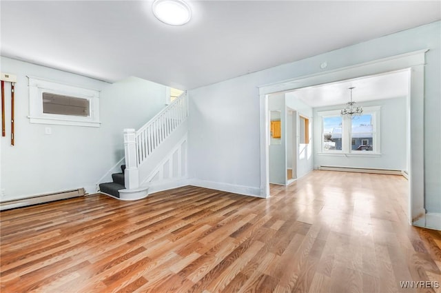 unfurnished living room with light wood-type flooring, stairway, a baseboard heating unit, and a notable chandelier