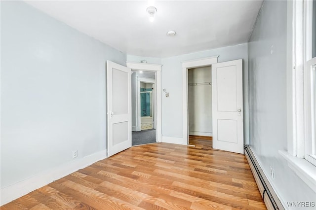 unfurnished bedroom with light wood-style floors, a baseboard radiator, a closet, and baseboards