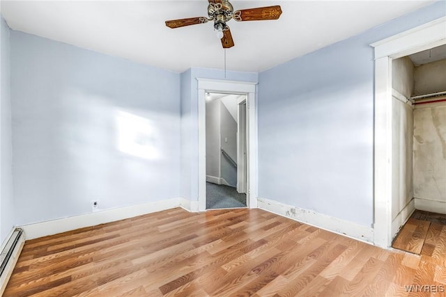 unfurnished bedroom featuring ceiling fan, baseboard heating, light wood-type flooring, and baseboards