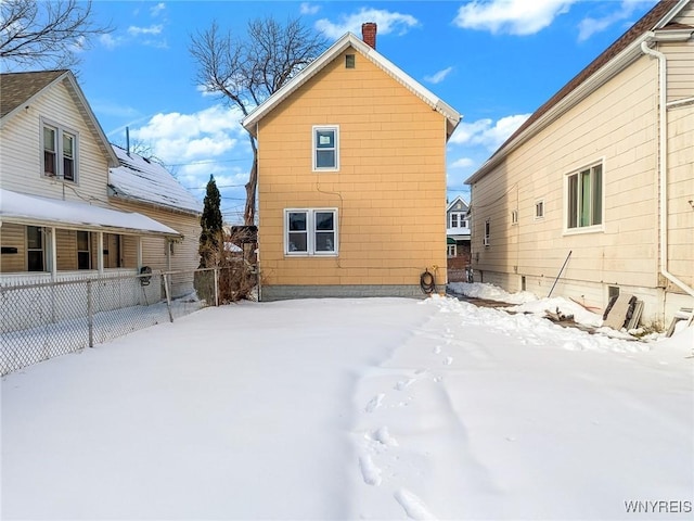 snow covered rear of property with fence and a chimney