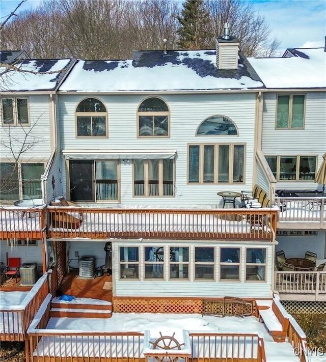 snow covered rear of property featuring a chimney and central AC unit