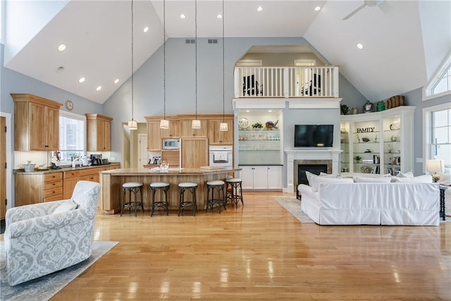 living room featuring visible vents, a ceiling fan, light wood-type flooring, a fireplace, and high vaulted ceiling