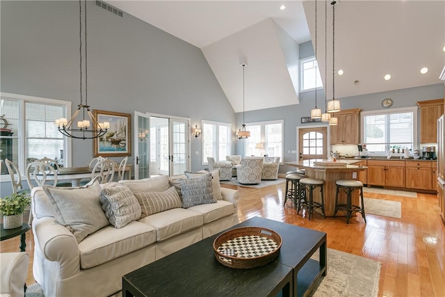 living room with a chandelier, high vaulted ceiling, visible vents, french doors, and light wood finished floors