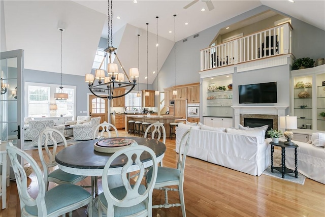 dining space featuring recessed lighting, ceiling fan with notable chandelier, a fireplace, a towering ceiling, and light wood finished floors