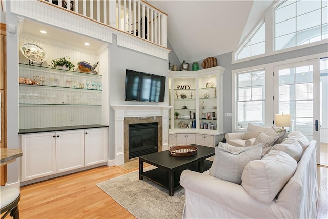 living area with high vaulted ceiling, a high end fireplace, and light wood-style flooring