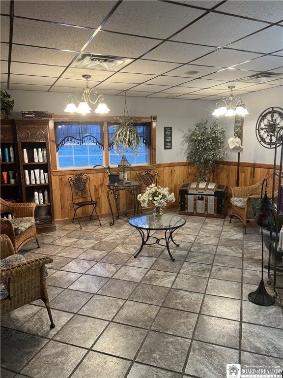 interior space featuring visible vents, an inviting chandelier, wainscoting, wooden walls, and a drop ceiling