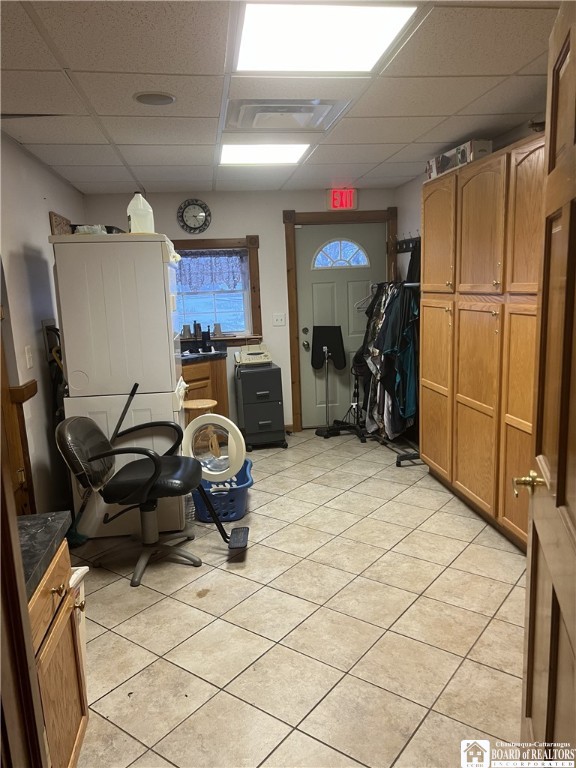 interior space featuring light tile patterned floors, dark countertops, visible vents, brown cabinetry, and a drop ceiling