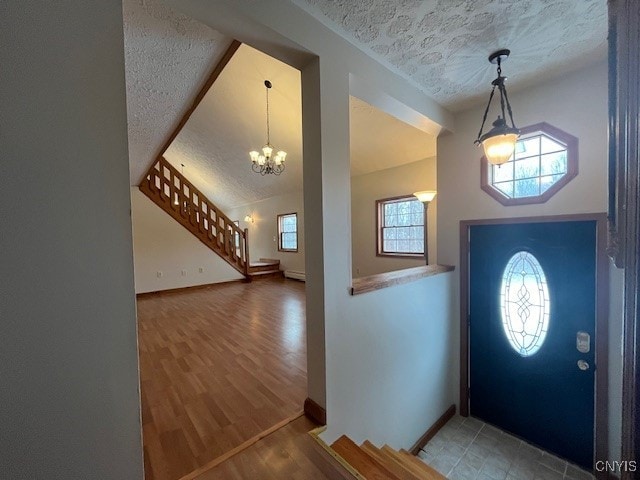 entryway featuring a textured ceiling, wood finished floors, baseboards, stairs, and vaulted ceiling