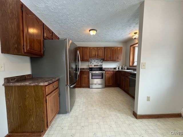 kitchen featuring a textured ceiling, light floors, appliances with stainless steel finishes, and dark countertops