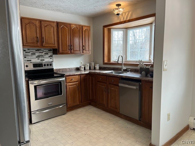 kitchen with stainless steel appliances, light floors, a sink, and brown cabinets