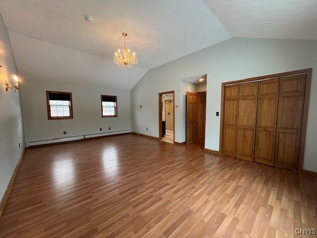 interior space with a textured ceiling, a notable chandelier, a baseboard heating unit, vaulted ceiling, and light wood-type flooring