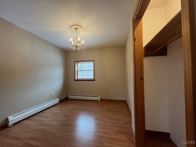 spare room featuring a baseboard heating unit, wood finished floors, and a notable chandelier