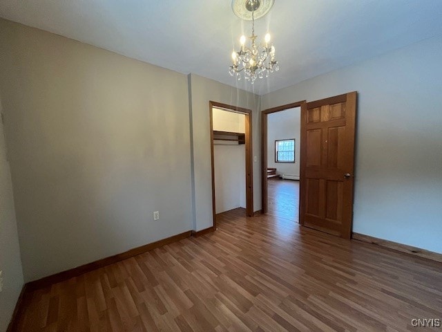 empty room with an inviting chandelier, baseboards, and wood finished floors