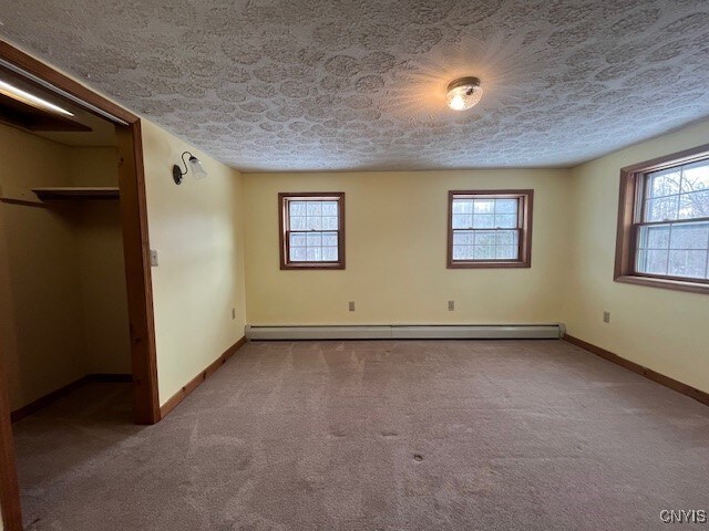 unfurnished bedroom with carpet floors, a baseboard radiator, baseboards, and a textured ceiling