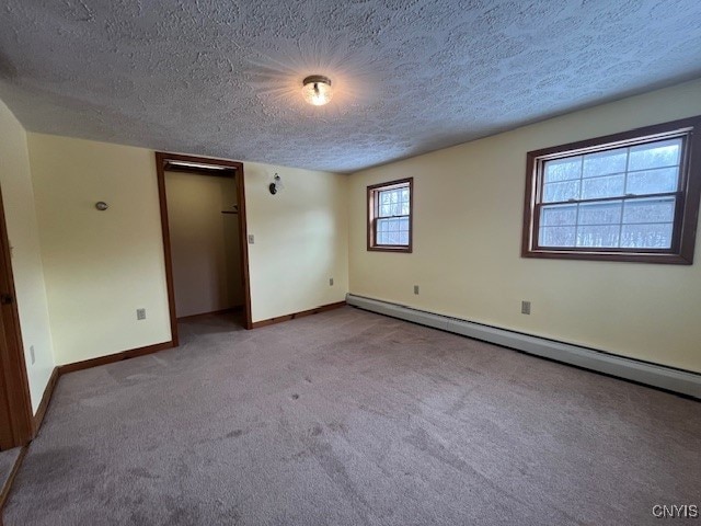 carpeted spare room with a baseboard heating unit, a textured ceiling, and baseboards