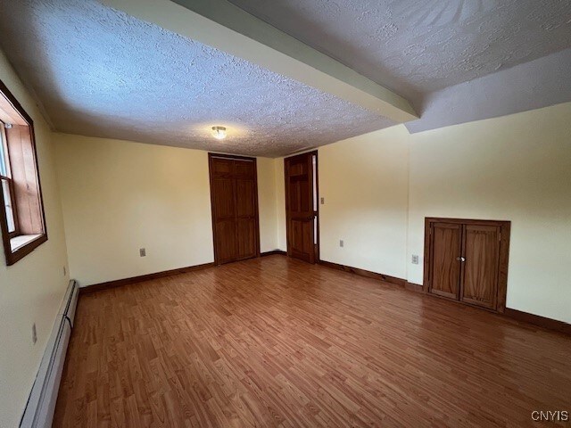 spare room featuring a baseboard heating unit, a textured ceiling, baseboards, and wood finished floors