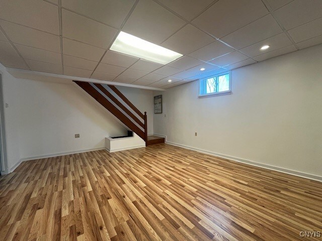 below grade area featuring a paneled ceiling, recessed lighting, wood finished floors, baseboards, and stairs