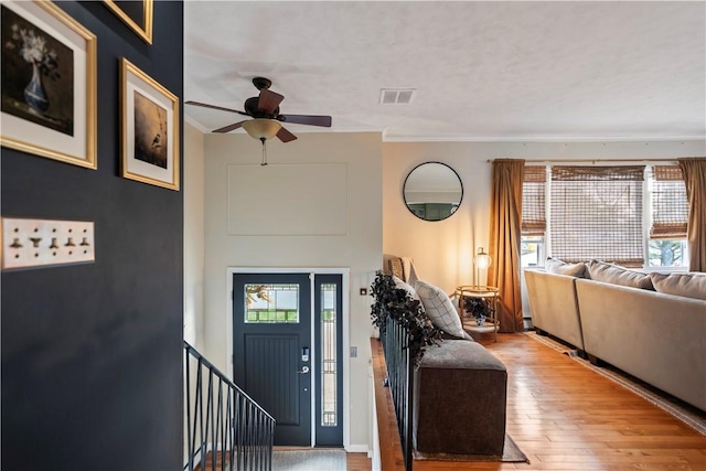 entrance foyer with wood-type flooring, visible vents, a ceiling fan, and ornamental molding