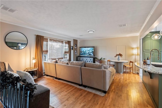 living room featuring light wood-type flooring, visible vents, and crown molding