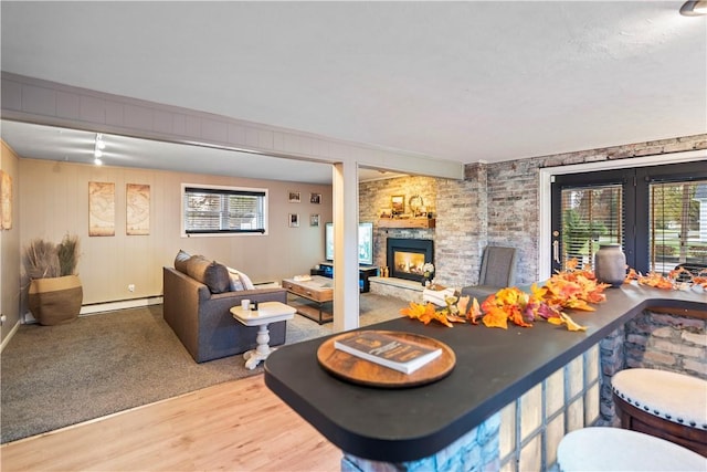 living area with wood finished floors, baseboard heating, a wealth of natural light, and a stone fireplace