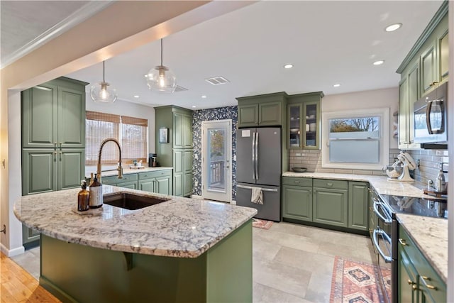 kitchen with backsplash, green cabinets, appliances with stainless steel finishes, a sink, and light stone countertops