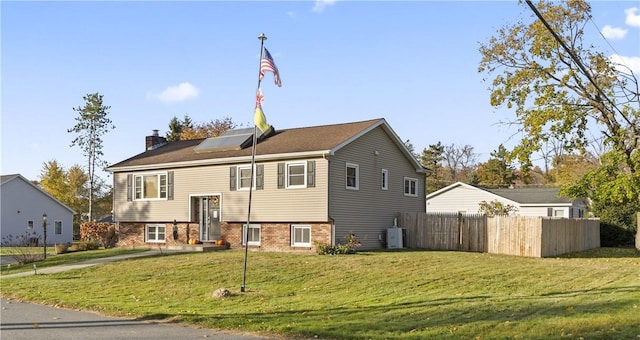 raised ranch with a chimney, solar panels, central AC unit, fence, and a front lawn